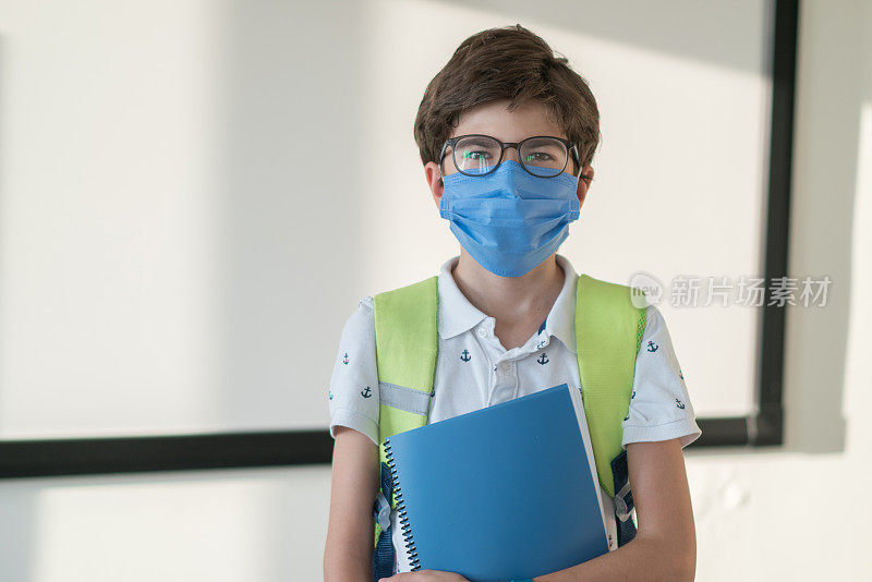 一名学童背着书包和书本戴口罩，防止Covid - 19疫情在教室爆发。